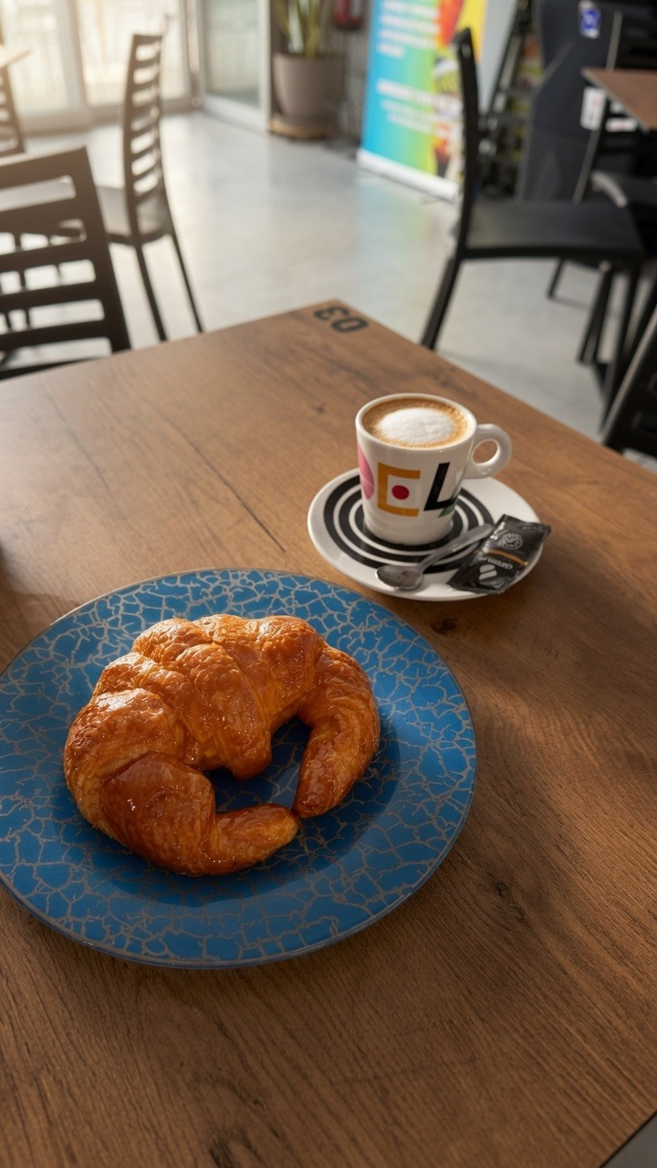 Croissant dorado en plato azul junto a un café con leche